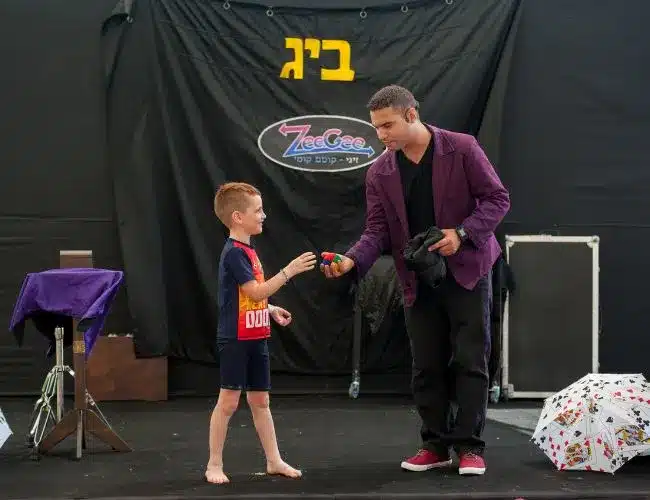 אמן חושים מגיש כדורי ספוג צבעוניים לילד במהלך מופע על במה